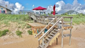 A wooden staircase leading to a beach area with a red umbrella and a thatched roof structure. - Beachside Cottage
 (Flagler Beach)