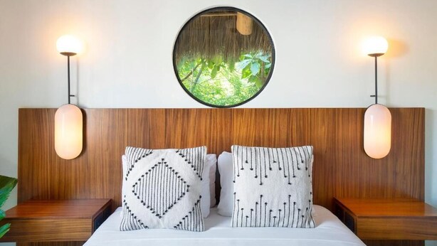 A bedroom with a wooden headboard, two bedside tables, a round mirror with a nature view, and patterned pillows. - Casa Pia Sayulita (Sayulita)