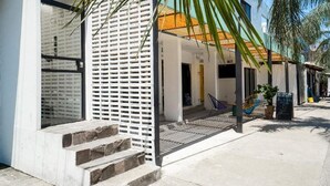A modern building with a white facade, a wooden slatted entrance, and a small outdoor seating area with a hammock and chairs. - Casa Pia Sayulita (Sayulita)