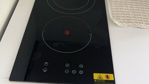 Et køkken med en sort induktionskogetop og en hvid elkedel på bordpladen.