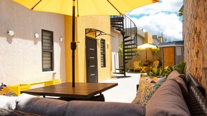 Um pátio externo com mesa de madeira, cadeiras amarelas e um sofá de vime.