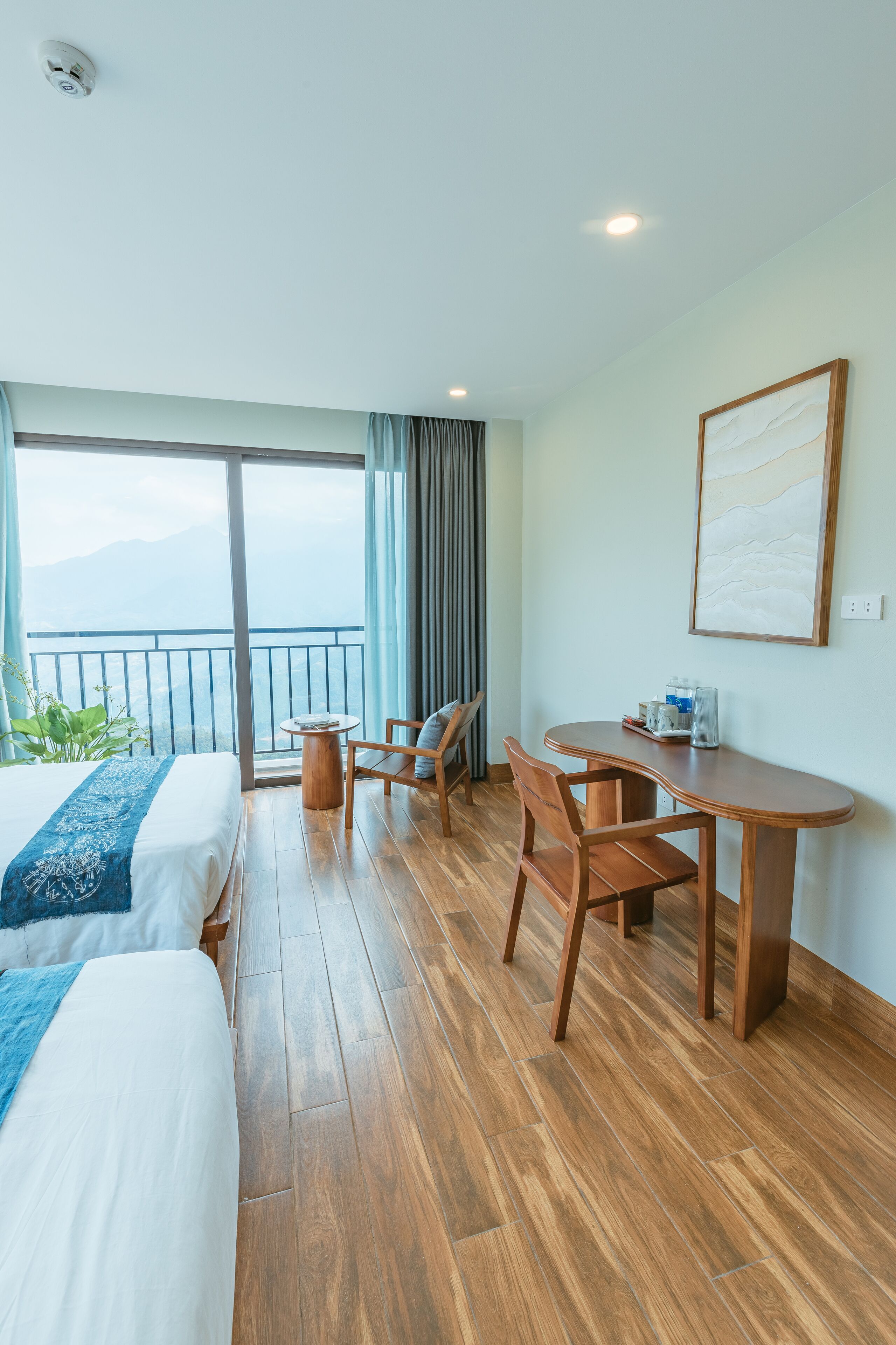 Een hotelkamer met een bed, een bureau, twee stoelen, een tafeltje, een raam met uitzicht op bergen en een schilderij aan de muur.