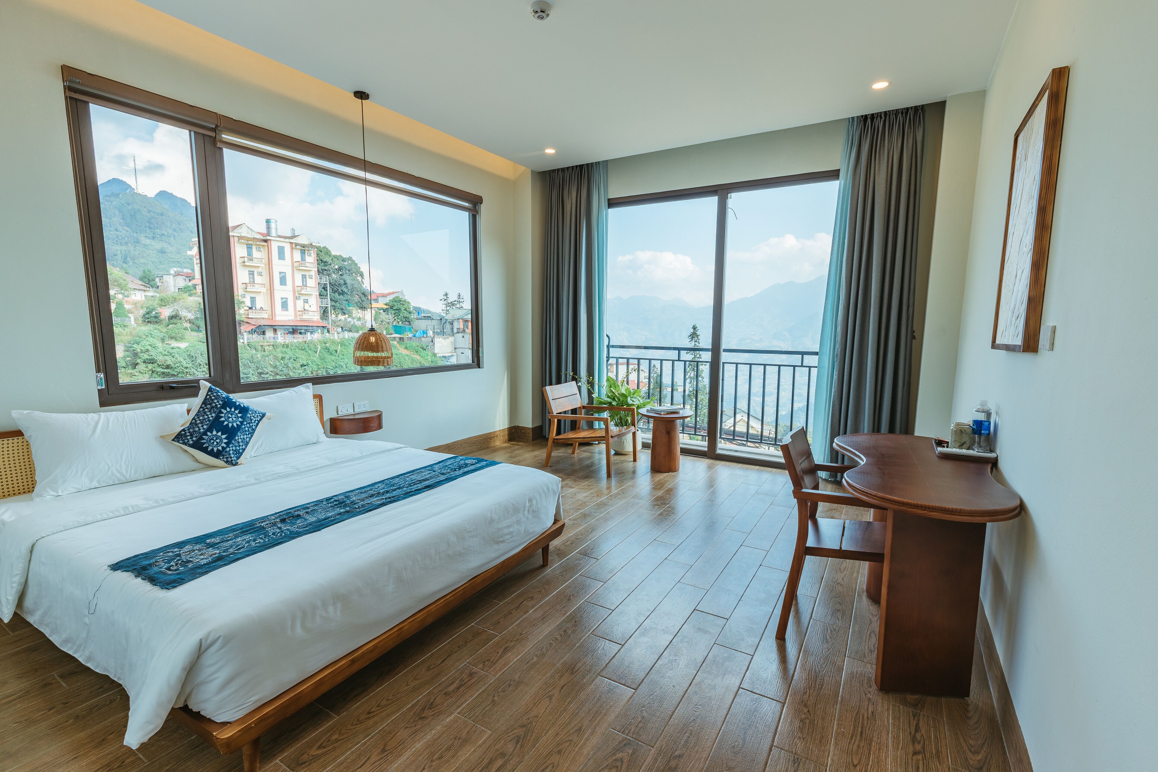 A spacious bedroom with a large bed, a desk, and a balcony with a view of mountains.
