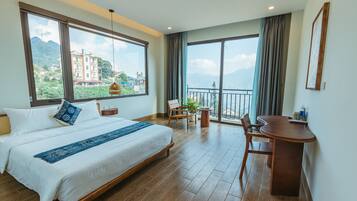A spacious bedroom with a large bed, a desk, and a balcony with a view of mountains.
