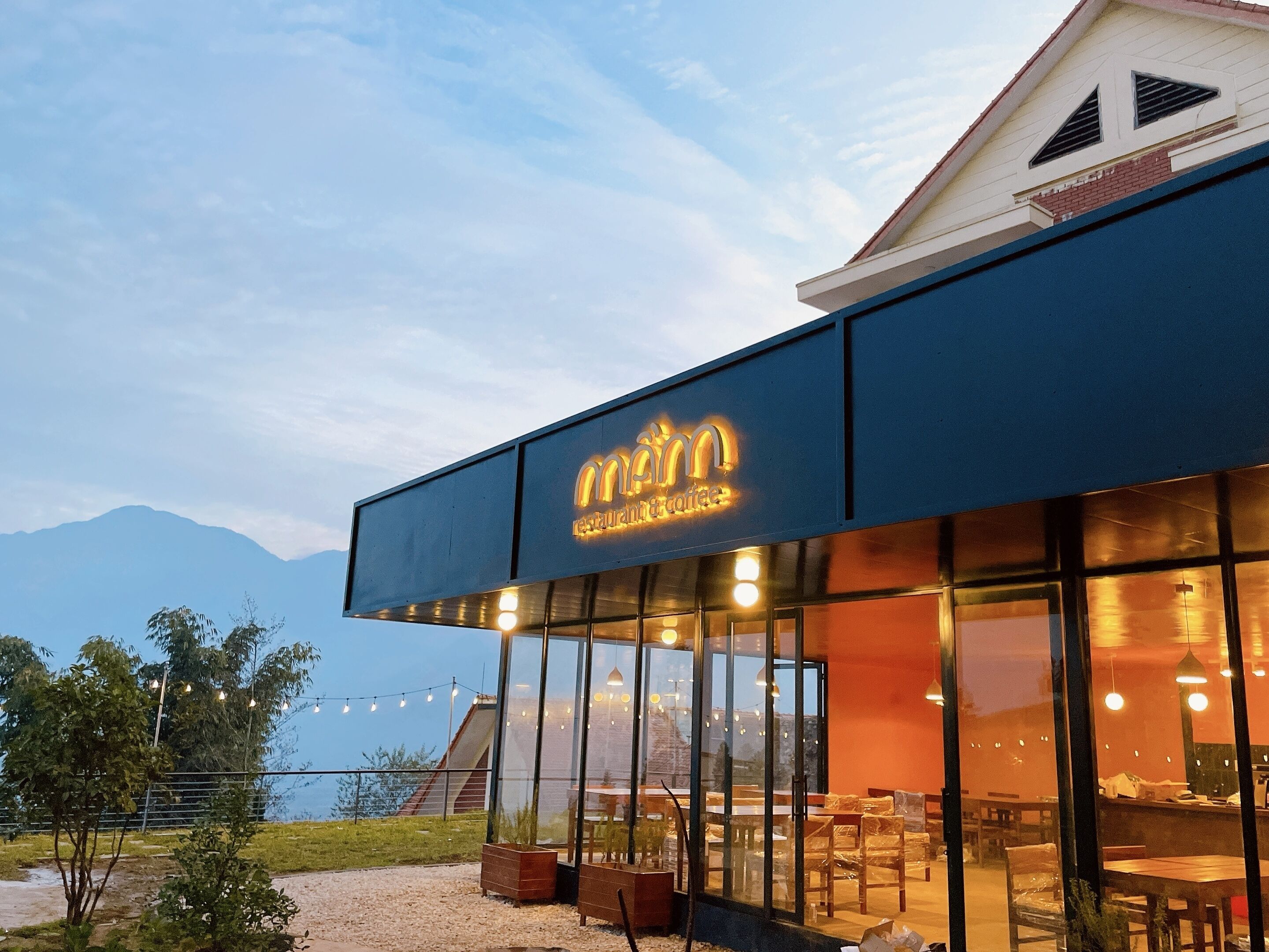 A restaurant with a modern glass facade and a mountain view in the background.