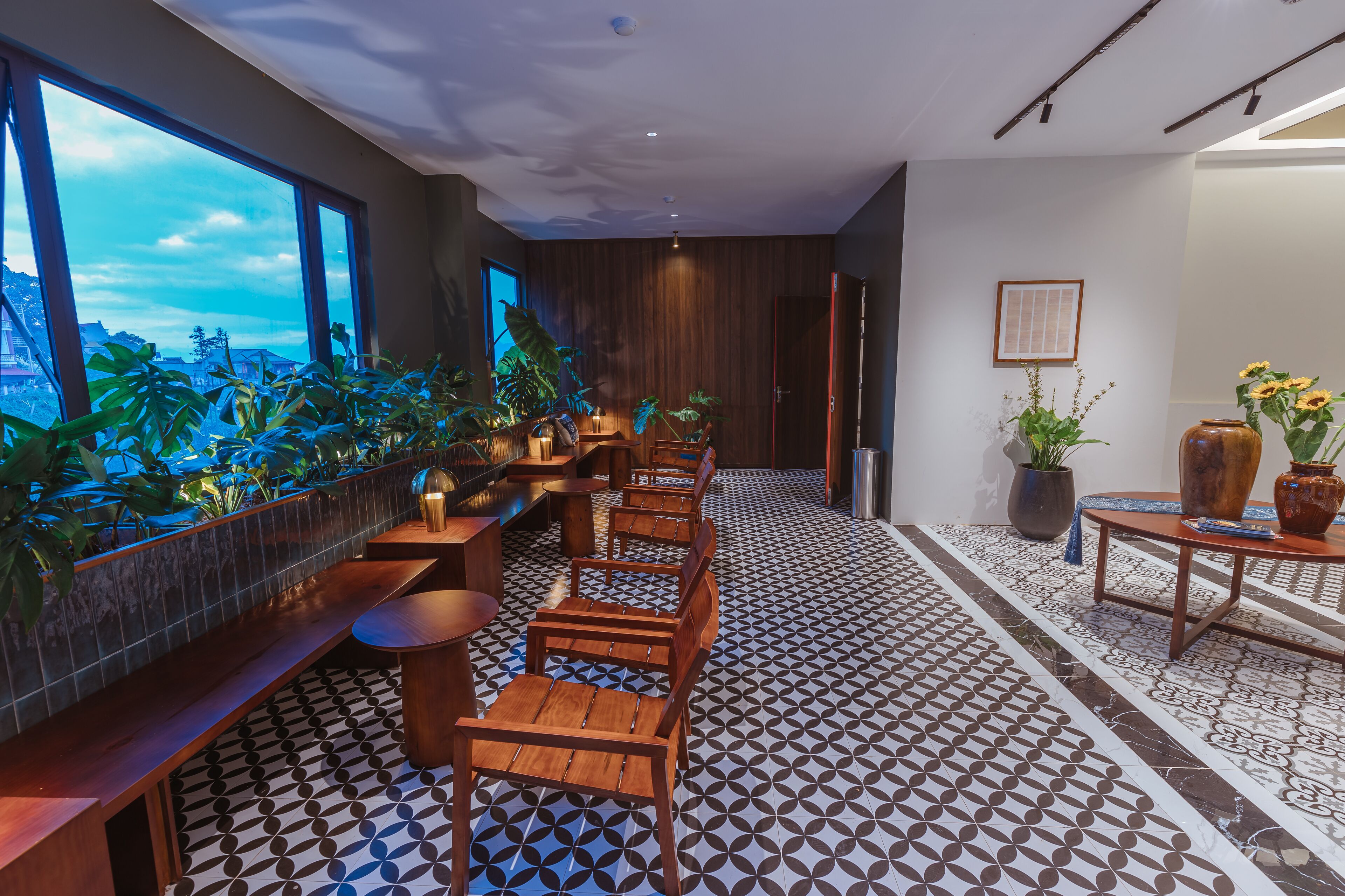 A modern interior with a long bench seating area, wooden tables, and potted plants.
