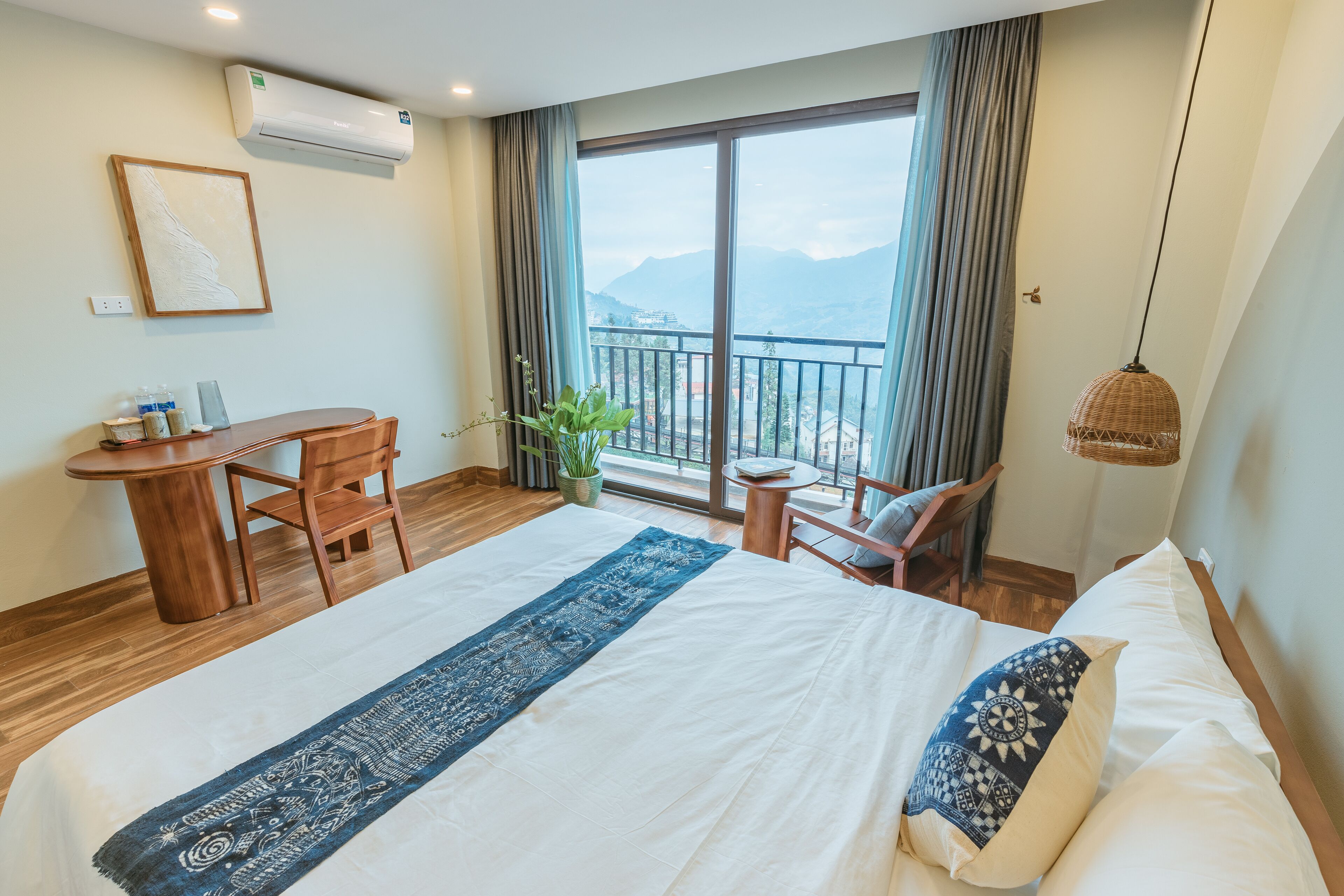 Une chambre d’hôtel avec un lit, un bureau, une chaise, une plante en pot et une vue sur les montagnes.