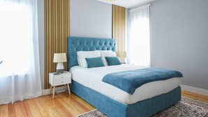 A bedroom with a blue bed, white nightstands, and a patterned rug. - Casa dos Infantes  (Vendas Novas)