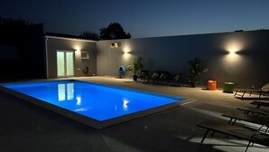 An outdoor swimming pool with a blue tint, surrounded by lounge chairs and a building with a door and windows. - Casa dos Infantes  (Vendas Novas)