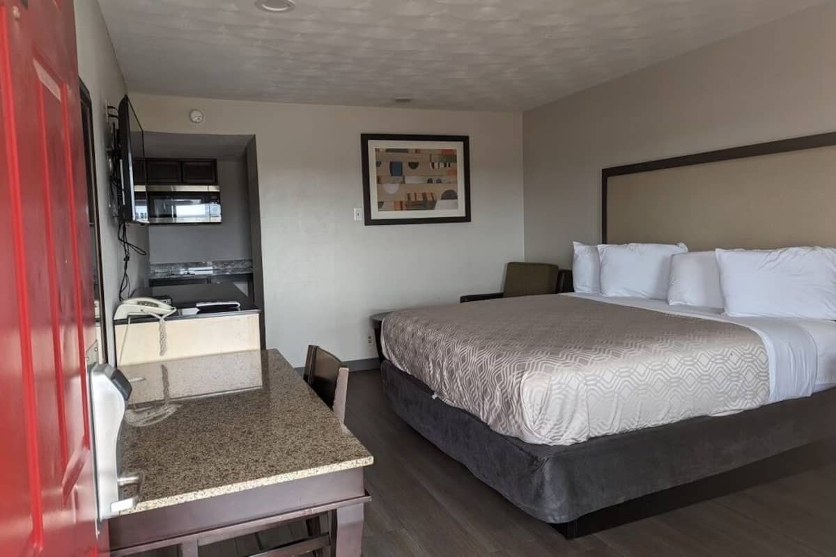 A hotel room with a bed, a desk, a chair, a TV, and a framed picture on the wall.