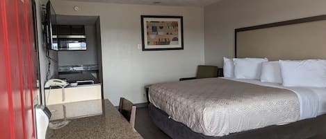 A hotel room with a bed, a desk, a chair, a TV, and a framed picture on the wall.