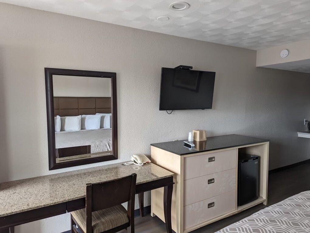 Habitación de hotel con cama, escritorio con silla, televisión, minibar y espejo.