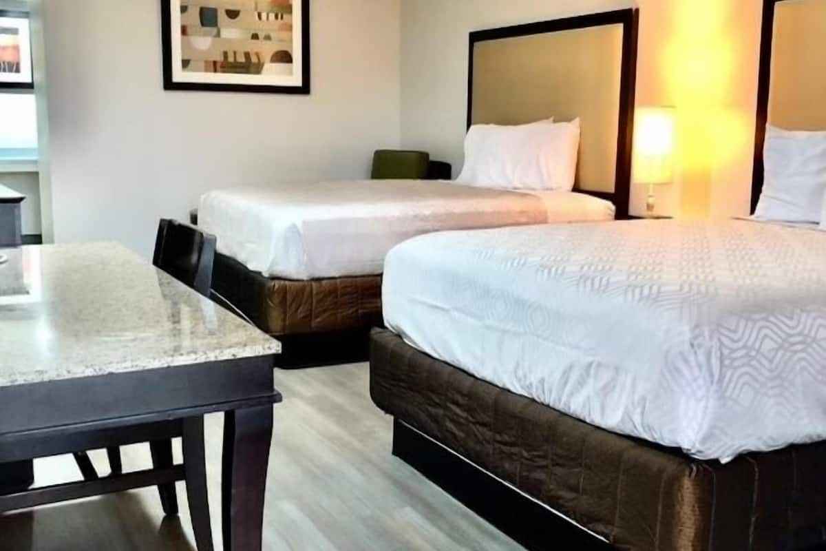 A hotel room with two beds, a desk, and a framed picture on the wall.