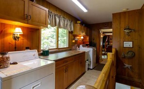 A kitchen with wooden cabinets, a washing machine, a refrigerator, and a window with curtains.