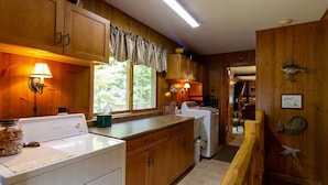 Una cocina con armarios de madera, lavadora, refrigerador y una ventana con cortinas.