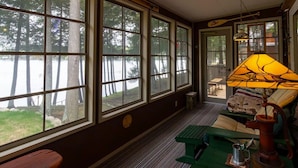 Un cuarto acogedor con ventanas amplias que dan a un bosque, un sofá verde, una lámpara y una mesita.