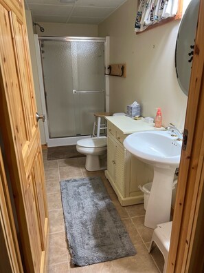 A bathroom with a shower, toilet, sink, and a small stool.