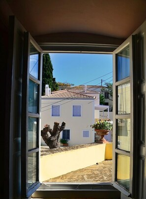 A view through an open window of a building with a tiled roof, a potted plant, and a tree trunk outside. - Villa Spetses 4BR downtown close to Agios Mamas Beach (Spetses)