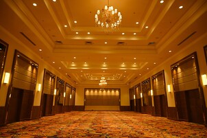 Un amplio vestíbulo de hotel con alfombra estampada, un candelabro y varias puertas.