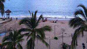 A beach with palm trees, a thatched hut, and people relaxing. - Breathtaking Ocean views in Central of Old Town in Puerto Vallarta. (Puerto Vallarta)