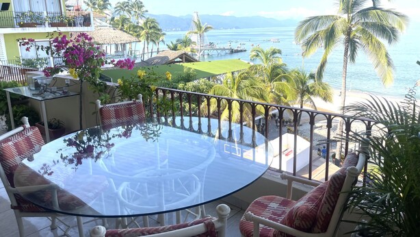 A glass-top table with chairs, a balcony with a railing, and a view of the sea and palm trees. - Breathtaking Ocean views in Central of Old Town in Puerto Vallarta. (Puerto Vallarta)
