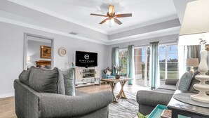 Ein modernes Wohnzimmer mit einem grauen Sofa, einem Couchtisch und einem Fernseher, der "Circular Hospitality" anzeigt.