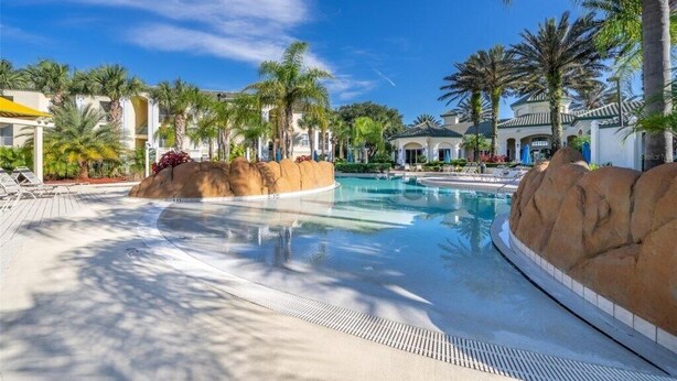 A resort pool area with palm trees, lounge chairs, and a clear blue sky.