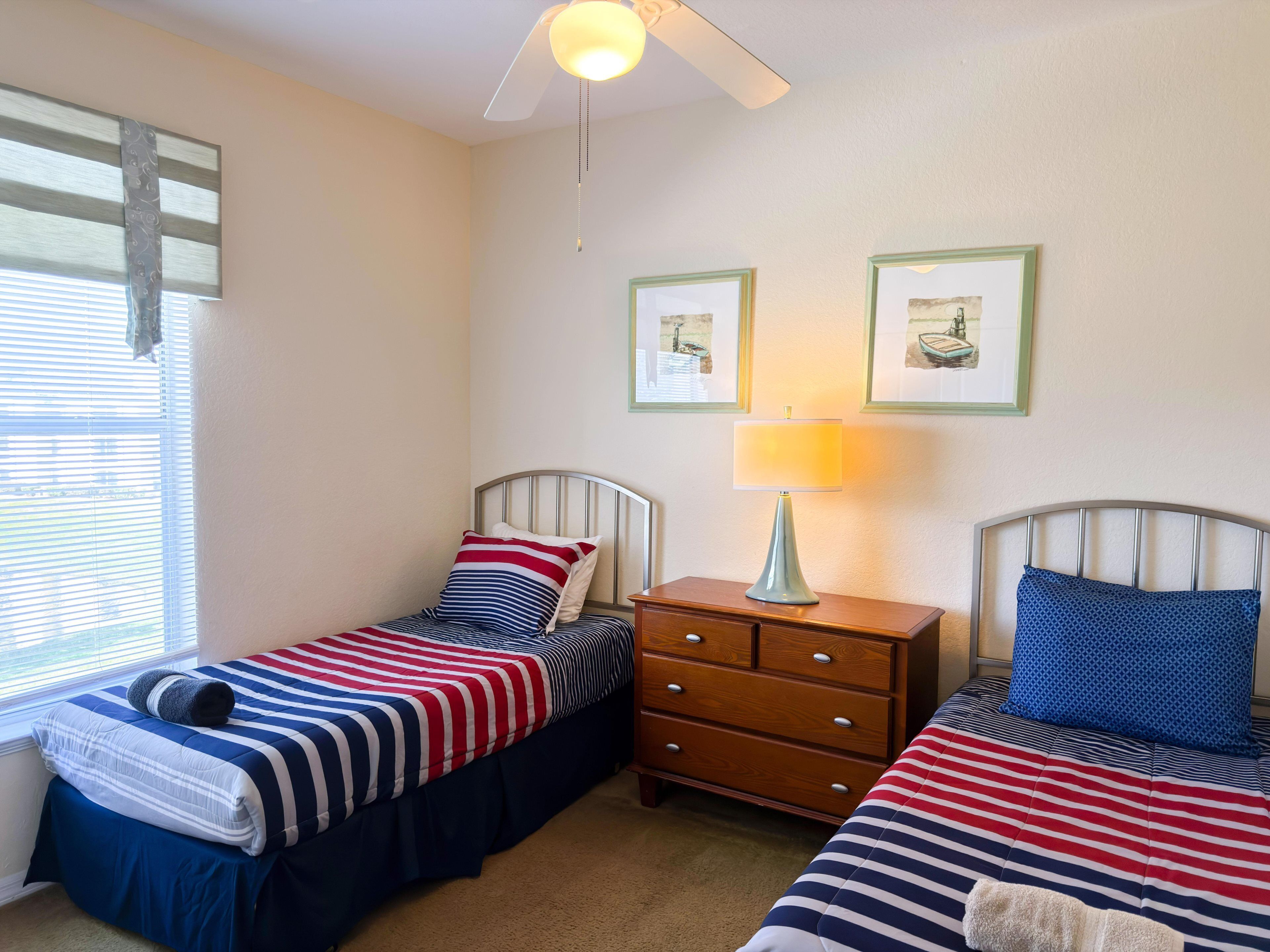 A bedroom with two single beds, a nightstand with a lamp, a dresser, and framed pictures on the wall.