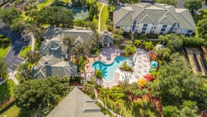 An aerial view of a resort with a swimming pool, palm trees, and a large building with a tiled roof.