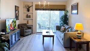 A living room with a television, sofa, coffee table, and a balcony with chairs.