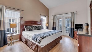 A hotel room with a large bed, a TV, a desk with a lamp, and a wardrobe.