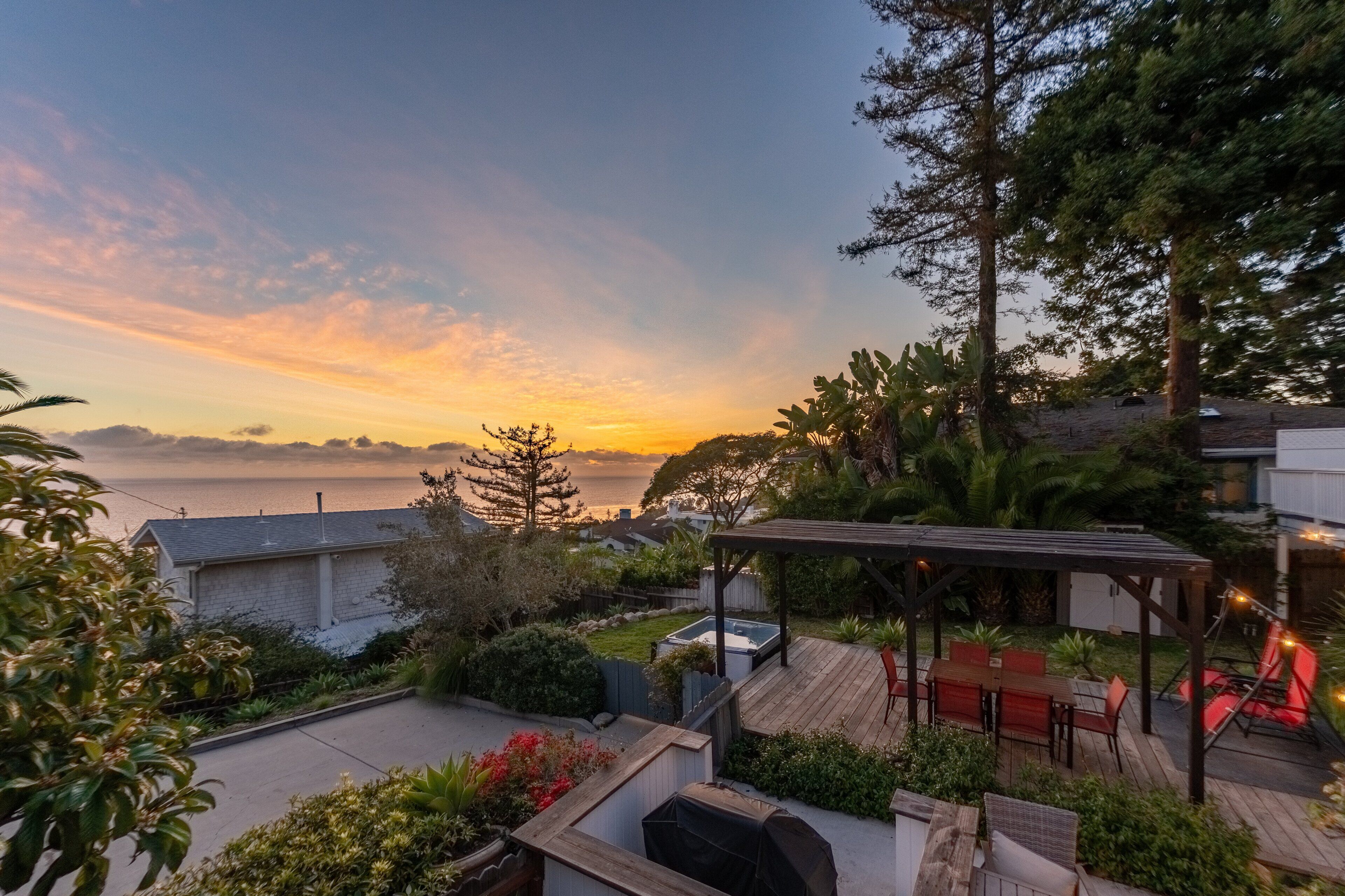 Un patio con mobiliario exterior, una terraza de madera y vista al océano al atardecer.