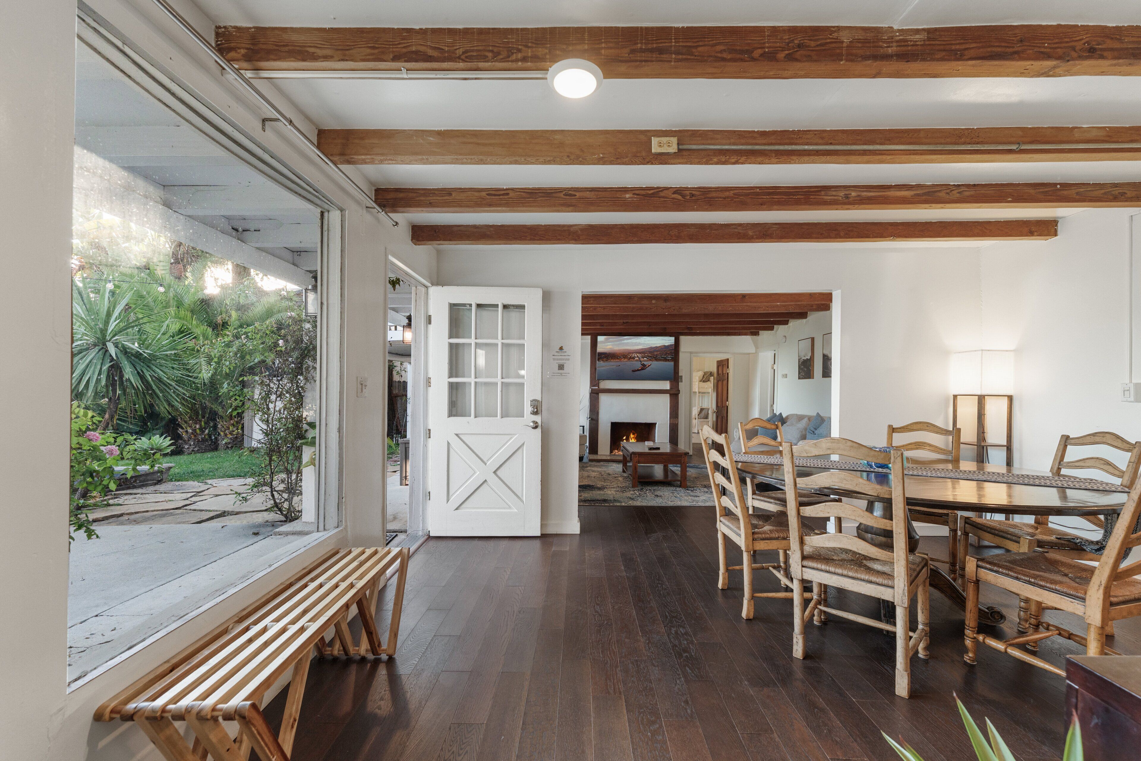 Un comedor con mesa y sillas de madera, un banco y vista a un jardín a través de un amplio ventanal.