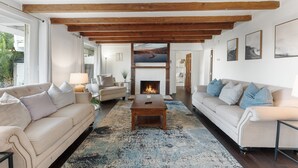 Una sala de estar con chimenea, sofás, una mesa de centro y vistas a través de un ventanal.