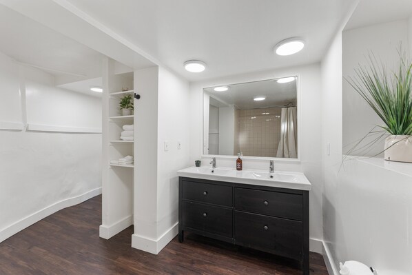 A bathroom with a white vanity, dark drawers, a mirror, and a plant. - 4BR Dog-Friendly Beach House | Hot Tub + Views (Summerland)