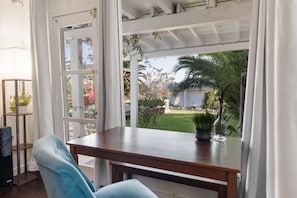 Ein Zimmer mit Holztisch, blauem Stuhl und Blick auf einen Garten durch ein Fenster.