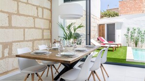 Un comedor con una mesa de madera dispuesta para seis personas, sillas blancas y una lámpara colgante grande de color blanco.