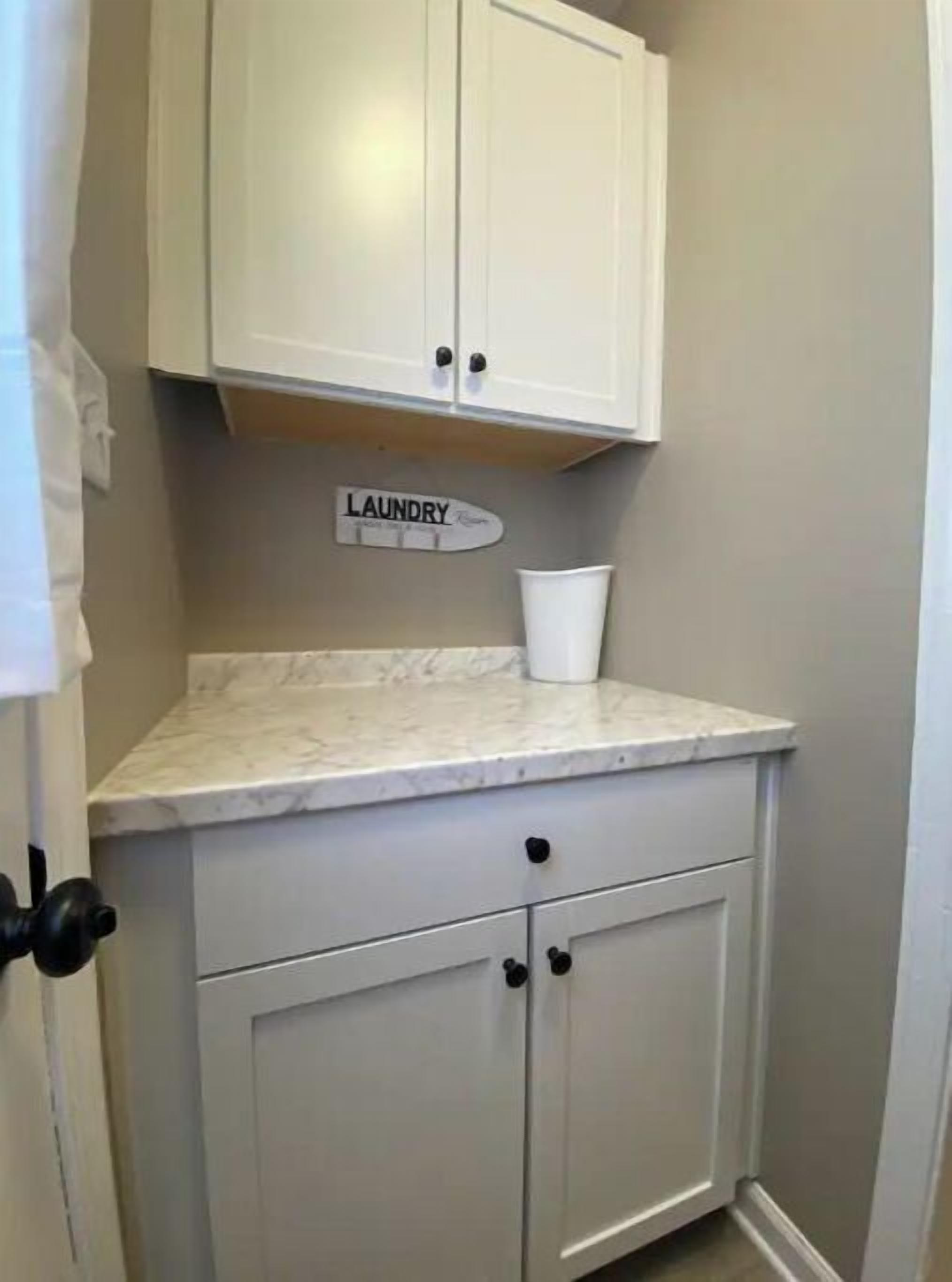 A laundry room with a marble countertop, a white cabinet, and a laundry sign.