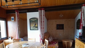 Un interior de madera con una mesa de comedor redonda, sillas con cojines azules, un sofá con un cubrecamas estampado y un televisor montado en la pared.