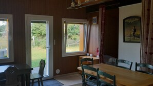 Un comedor con una mesa y sillas de madera, dos ventanas con cortinas y vistas a un jardín cubierto de césped.