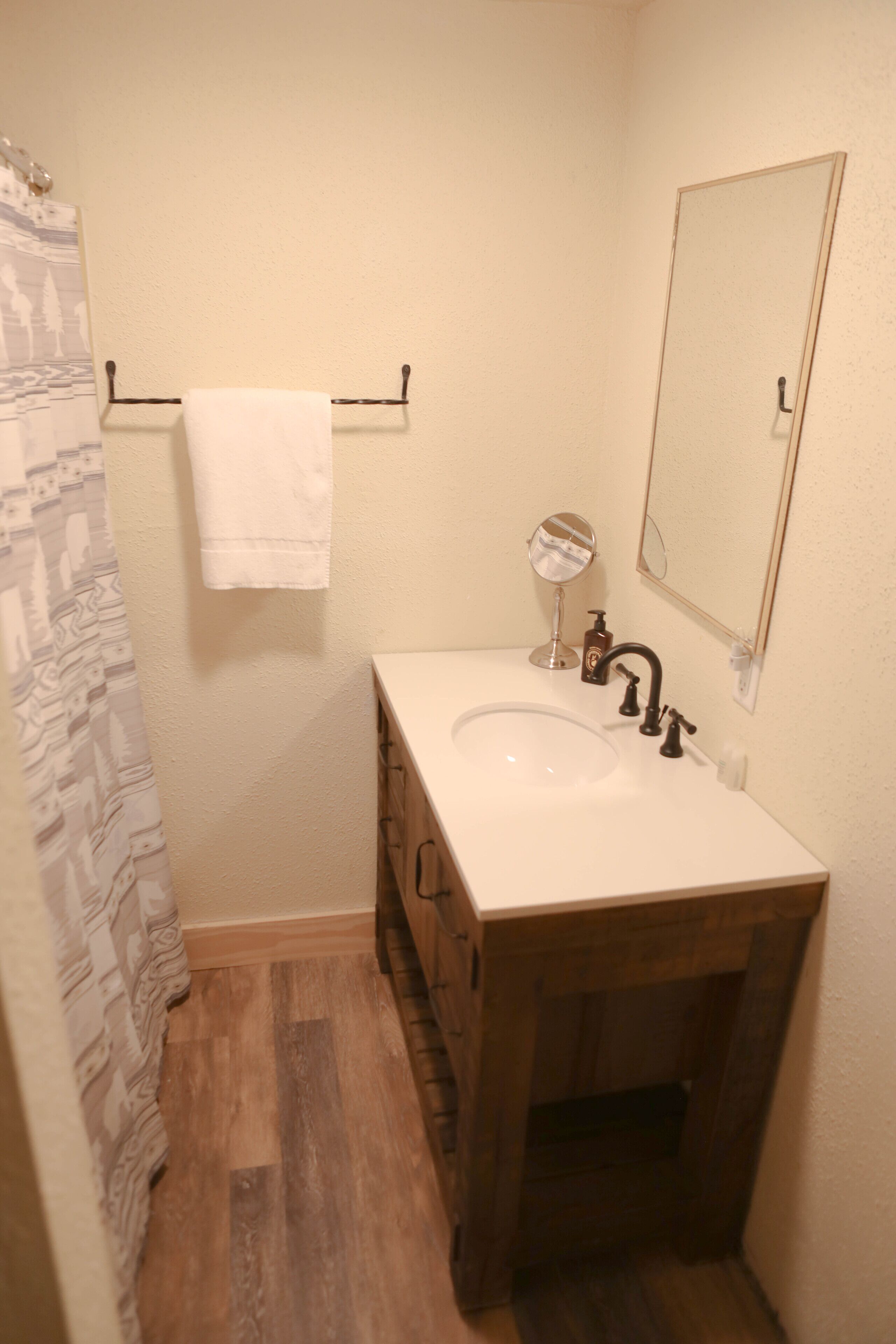 Un baño con tocador de madera, un lavabo blanco, un espejo y una toalla colgada en un perchero.