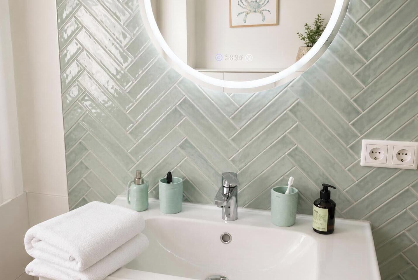 Un baño con pared de azulejos en patrón de espiga, un lavabo blanco con grifo moderno y un espejo sobre el lavabo.