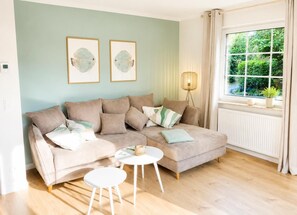 Un salon moderne avec un canapé beige, une petite table blanche et deux tableaux représentant des poissons, encadrés et accrochés au mur.
