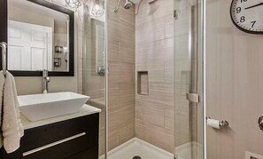 Bathroom features a sleek vessel sink, glass-enclosed shower, and light-colored tiles.