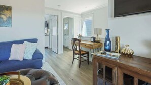 A living room with a blue sofa, a wooden dining table, and a TV mounted on the wall.