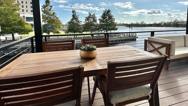 A wooden deck with a table and chairs, overlooking a body of water and trees.
