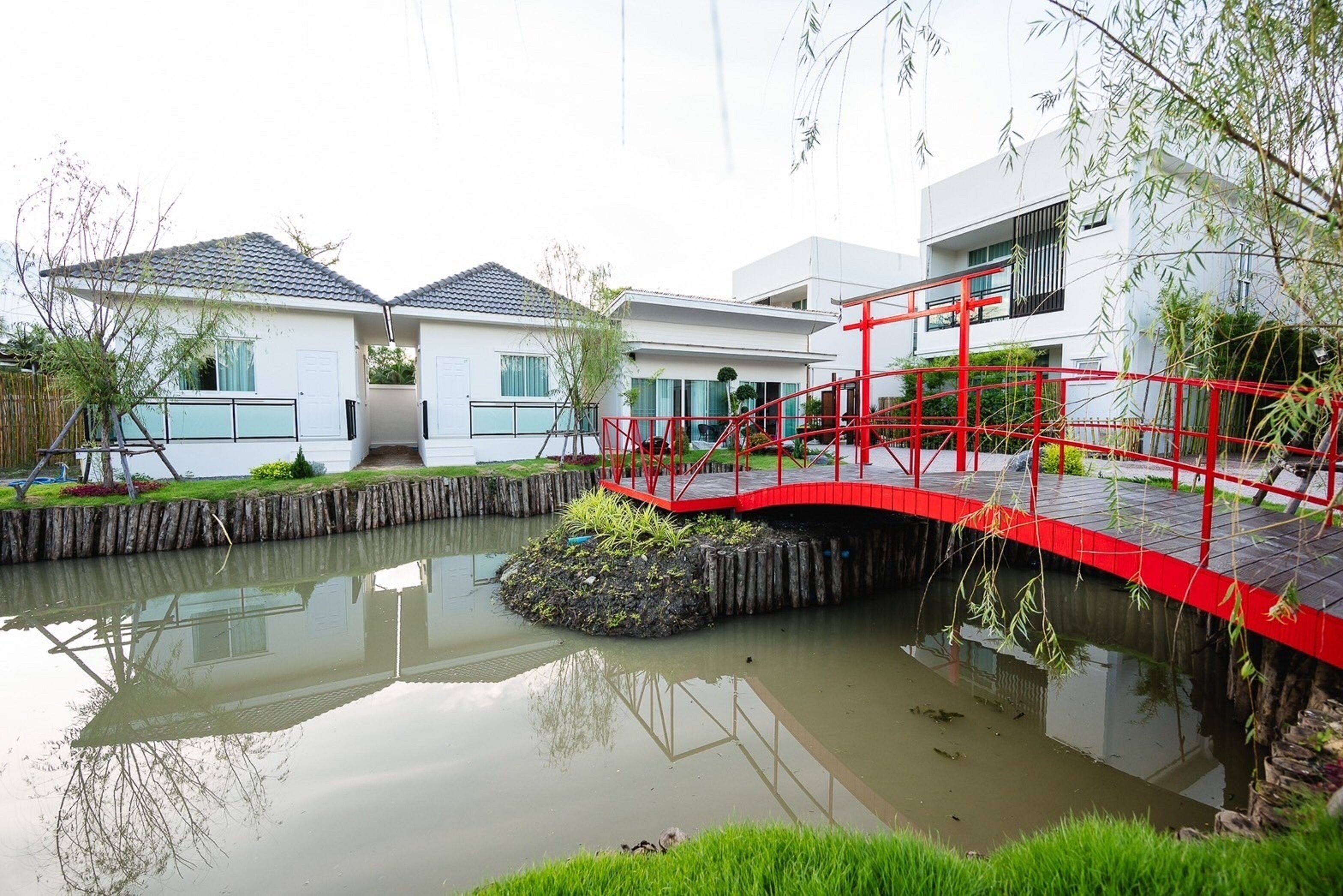 A modern residential area with a small pond, a red bridge, and white houses with balconies.