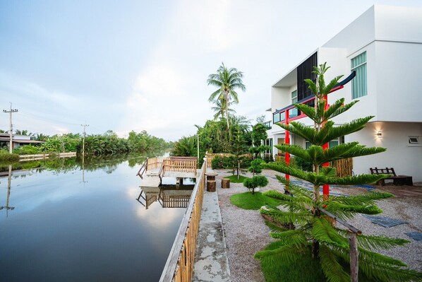 A modern building with a reflective water body in front, surrounded by greenery and a wooden deck.
