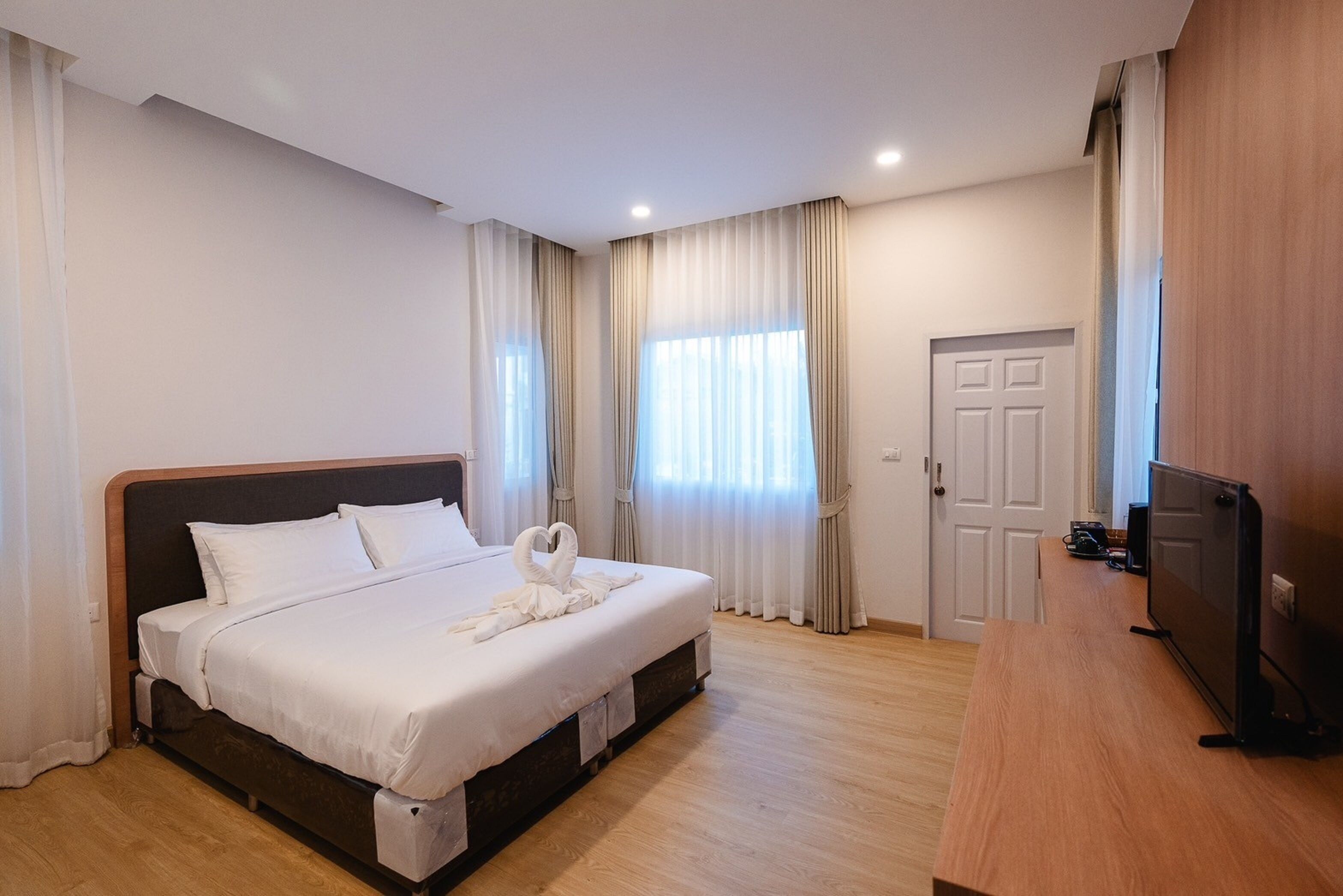 A hotel room with a large bed, a wooden desk, a television, and a door.