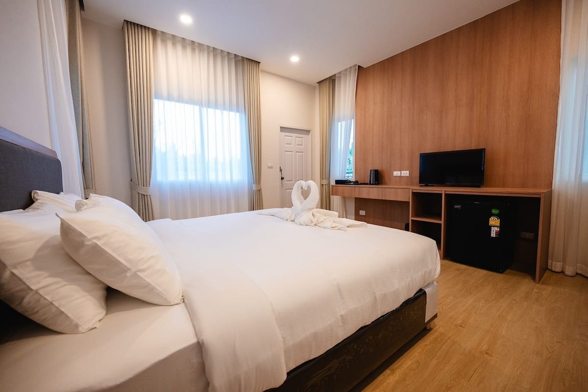 Habitación de hotel con una cama grande, televisión, minibar y paneles de madera en las paredes.